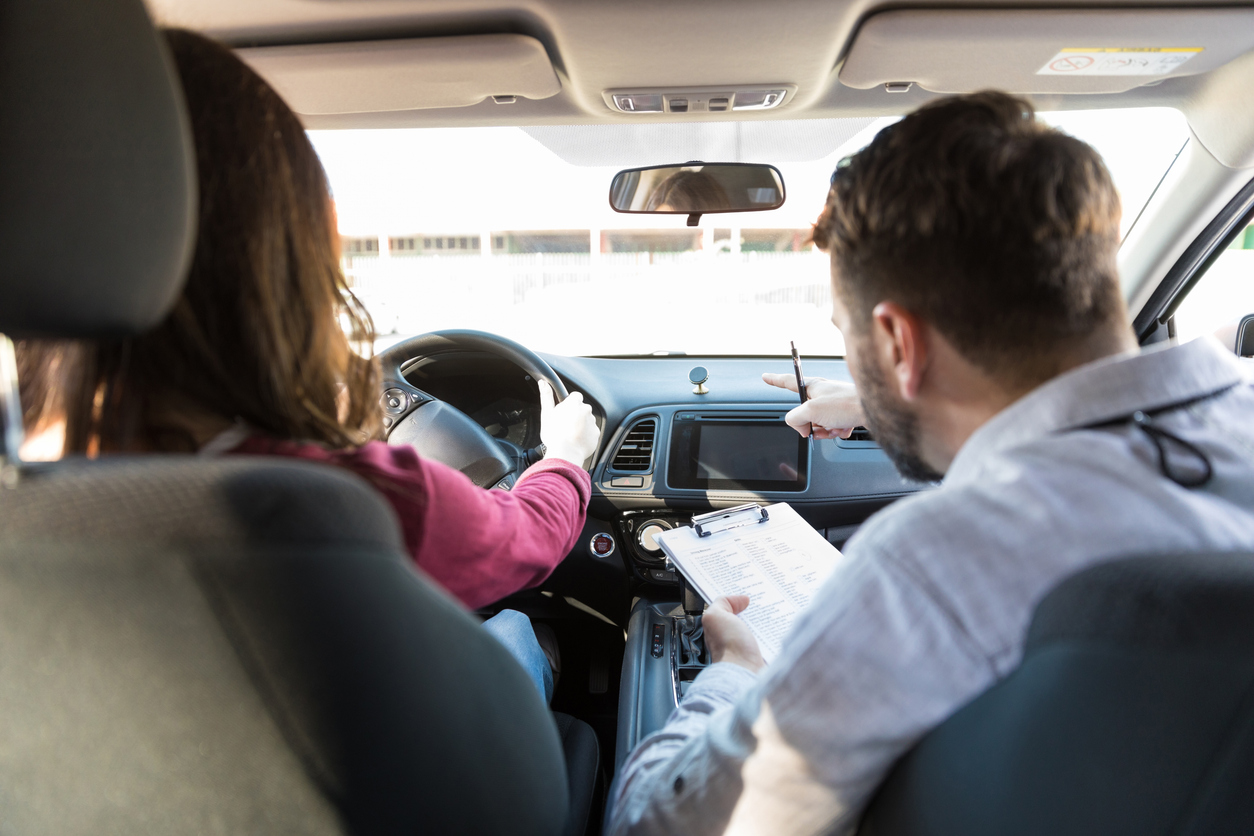 Fahrlehrer erklärt einer Fahrschülerin während der praktischen Autofahrstunde die Bedienung